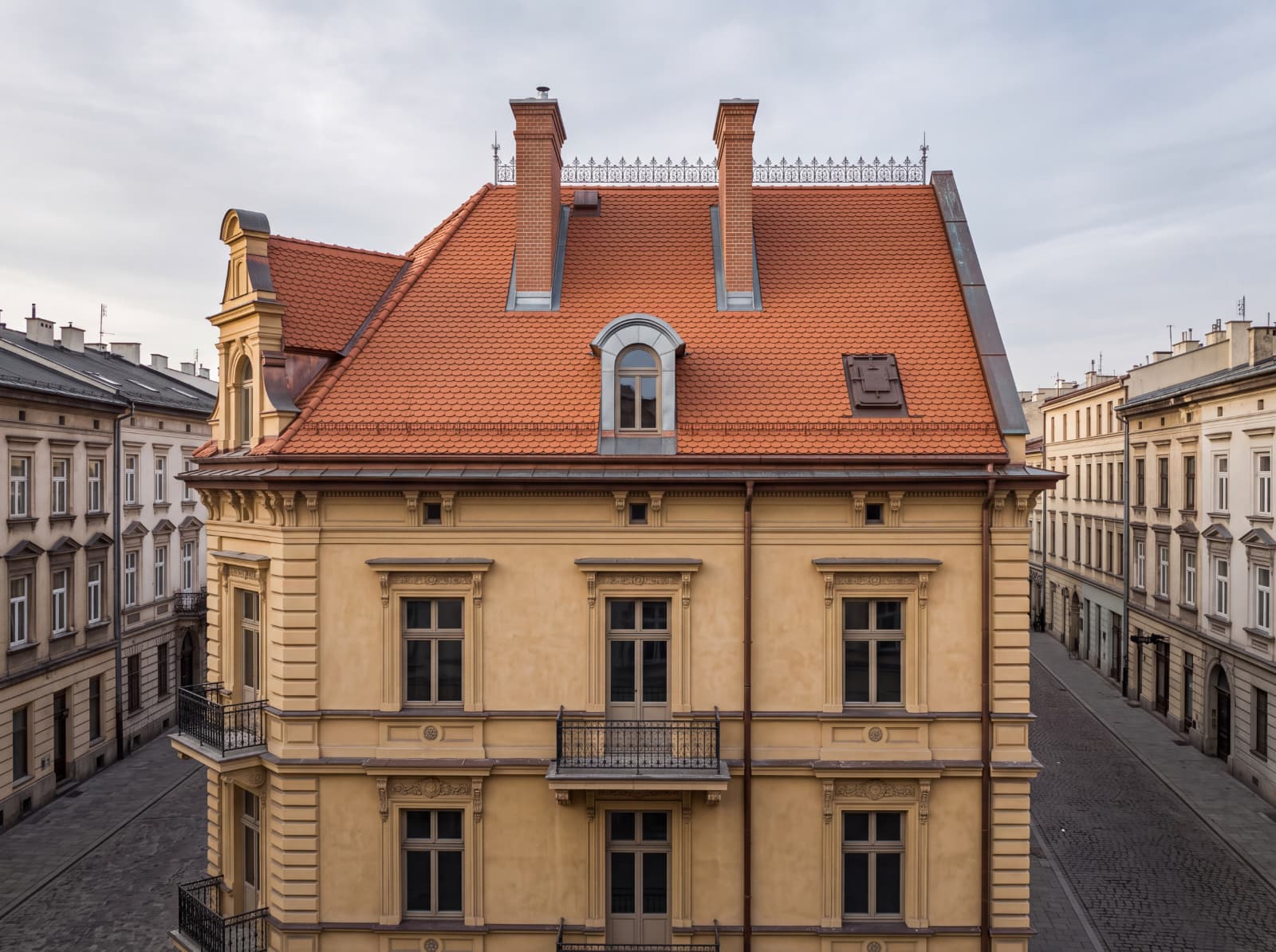 Odnowiony dach mansardowy kamienicy kryty dachówką karpiówką, z lukarną i dwoma kominami, Kraków